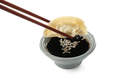 Photo of Dipping tasty gyoza (dumpling) into soy sauce on white background