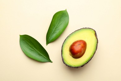 Photo of One cut ripe avocado and leaves on beige background, top view