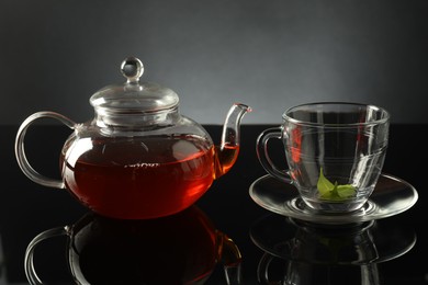 Photo of Teapot with freshly brewed tea and glass cup on black table, closeup
