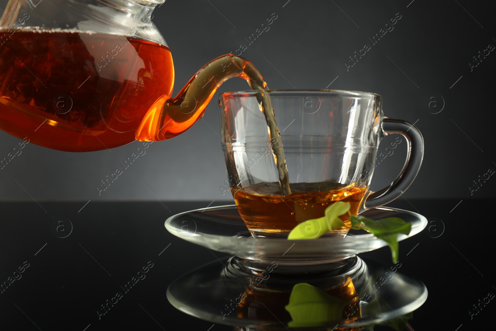 Pouring freshly brewed tea from teapot into glass cup on black table, closeup Photo of Pouring freshly brewed tea from teapot into glass cup on black table, closeup