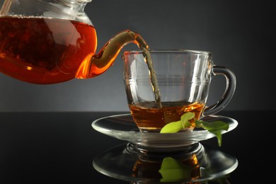 Photo of Pouring freshly brewed tea from teapot into glass cup on black table, closeup
