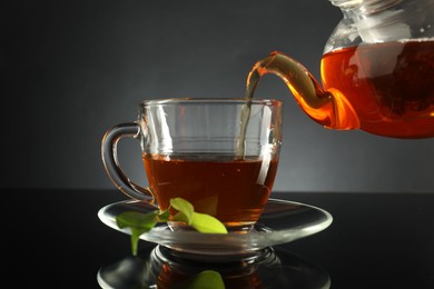 Photo of Pouring freshly brewed tea from teapot into glass cup on black table, closeup