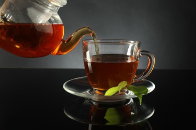 Photo of Pouring freshly brewed tea from teapot into glass cup on black table, closeup