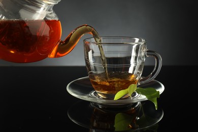 Photo of Pouring freshly brewed tea from teapot into glass cup on black table, closeup