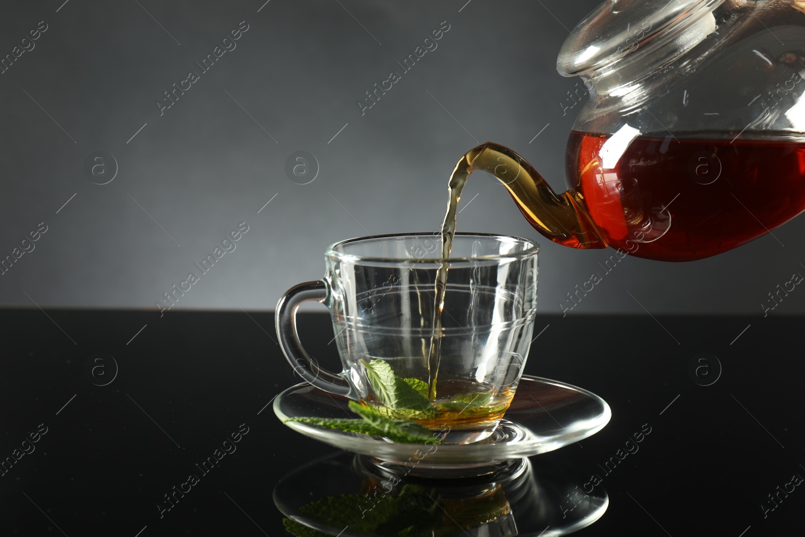 Pouring freshly brewed tea from teapot into cup at dark mirror table, closeup Photo of Pouring freshly brewed tea from teapot into cup at dark mirror table, closeup
