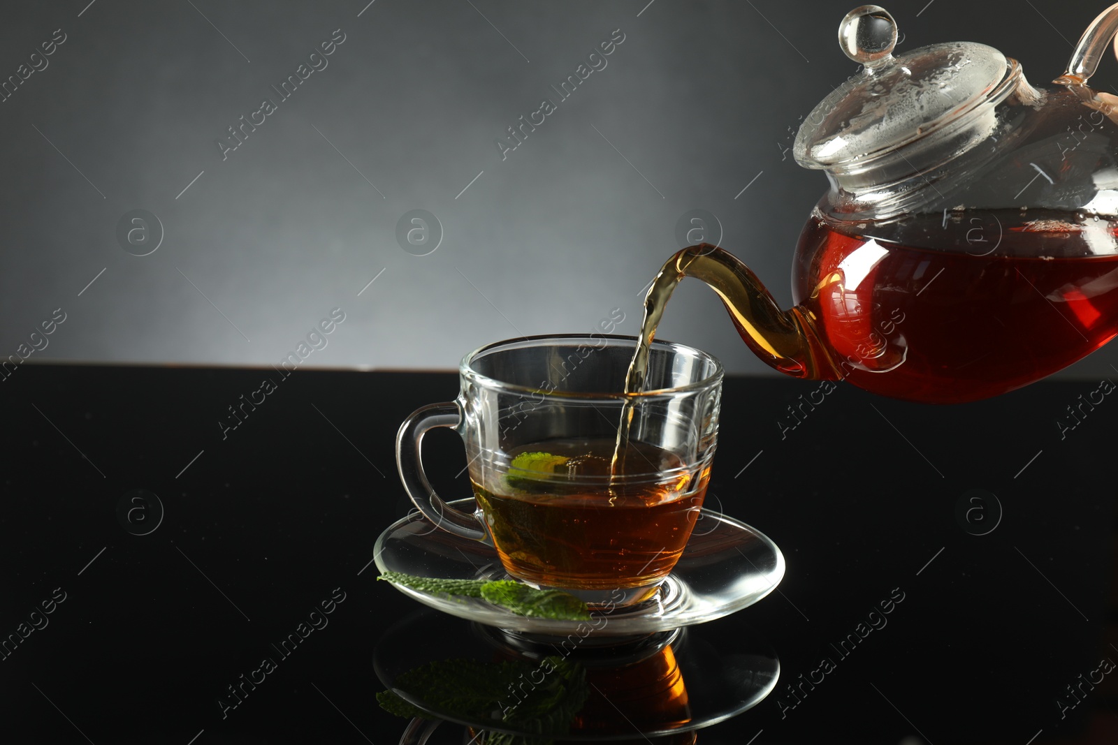 Pouring freshly brewed tea from teapot into cup at dark mirror table, closeup Photo of Pouring freshly brewed tea from teapot into cup at dark mirror table, closeup