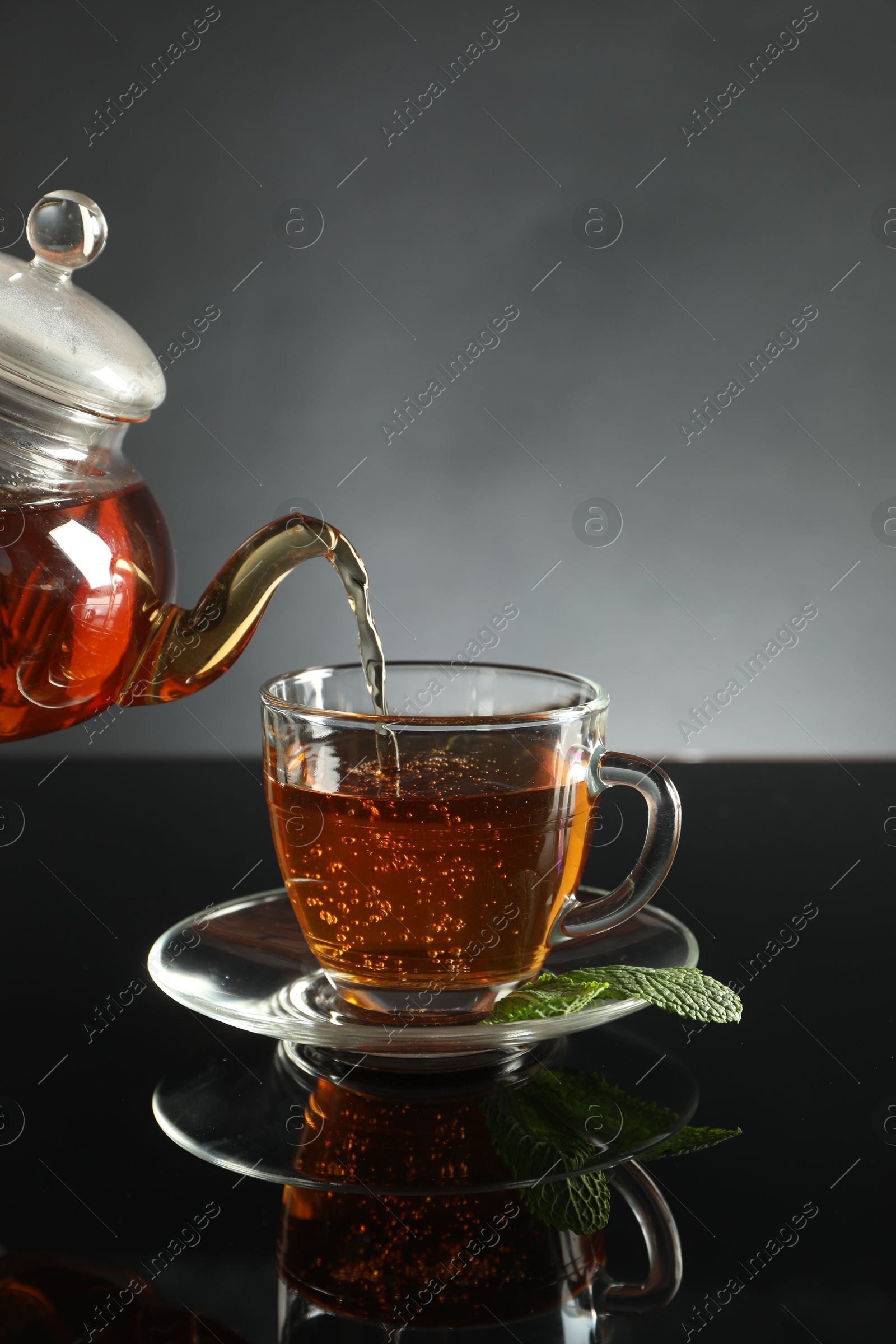 Pouring freshly brewed tea from teapot into cup at dark mirror table, closeup Photo of Pouring freshly brewed tea from teapot into cup at dark mirror table, closeup