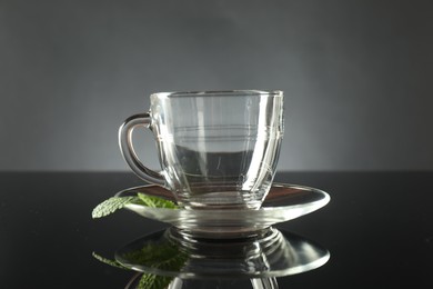 Photo of Glass cup, saucer and mint on dark mirror table