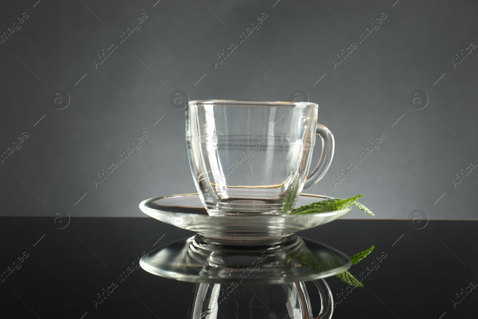 Glass cup, saucer and mint on dark mirror table Photo of Glass cup, saucer and mint on dark mirror table