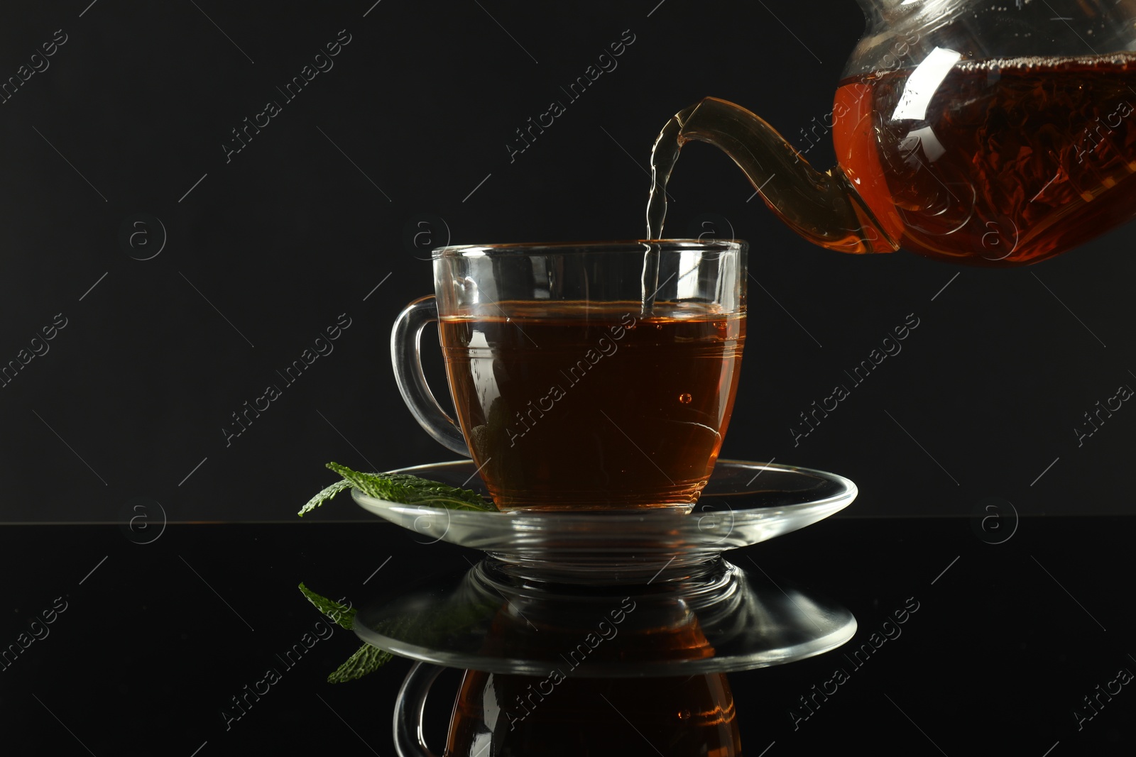 Pouring freshly brewed tea from teapot into cup at dark mirror table, closeup Photo of Pouring freshly brewed tea from teapot into cup at dark mirror table, closeup