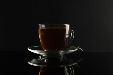 Photo of Aromatic tea in glass cup and mint on dark mirror table