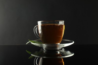 Photo of Aromatic tea in glass cup and mint on dark mirror table