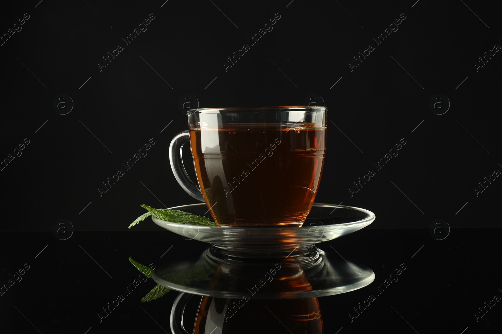 Aromatic tea in glass cup and mint on dark mirror table Photo of Aromatic tea in glass cup and mint on dark mirror table