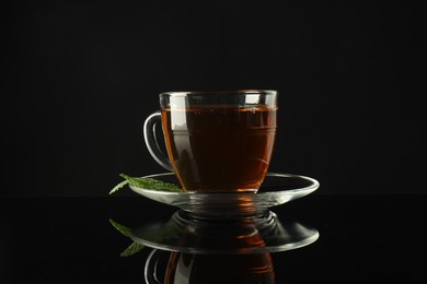 Photo of Aromatic tea in glass cup and mint on dark mirror table