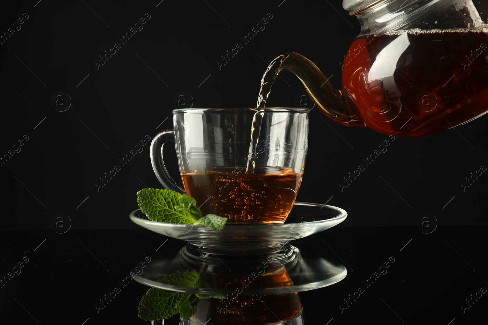 Pouring freshly brewed tea from teapot into cup at dark mirror table, closeup Photo of Pouring freshly brewed tea from teapot into cup at dark mirror table, closeup