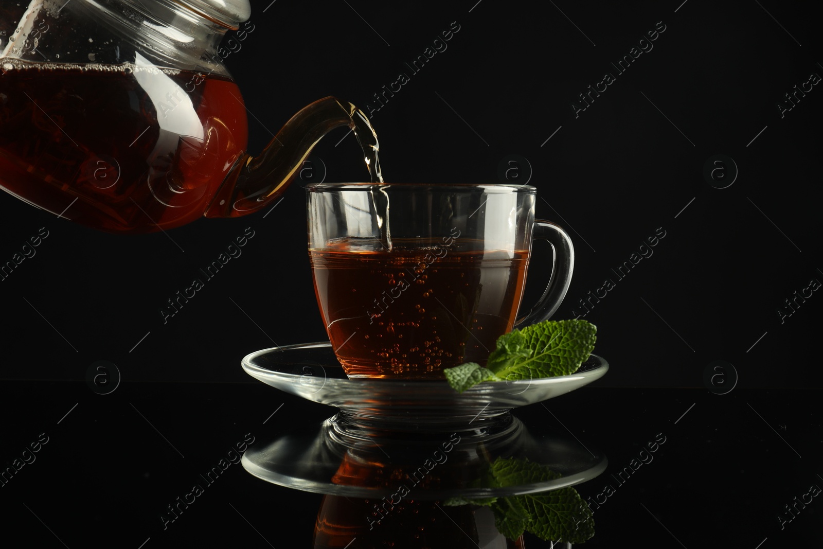 Pouring freshly brewed tea from teapot into cup at dark mirror table, closeup Photo of Pouring freshly brewed tea from teapot into cup at dark mirror table, closeup