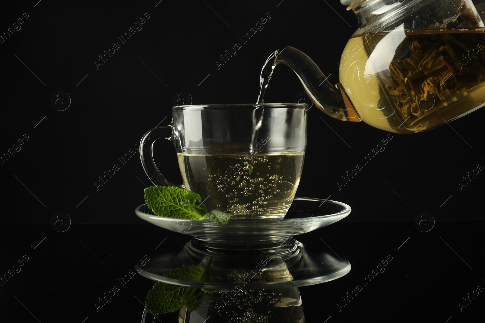 Pouring freshly brewed tea from teapot into cup at dark mirror table, closeup Photo of Pouring freshly brewed tea from teapot into cup at dark mirror table, closeup