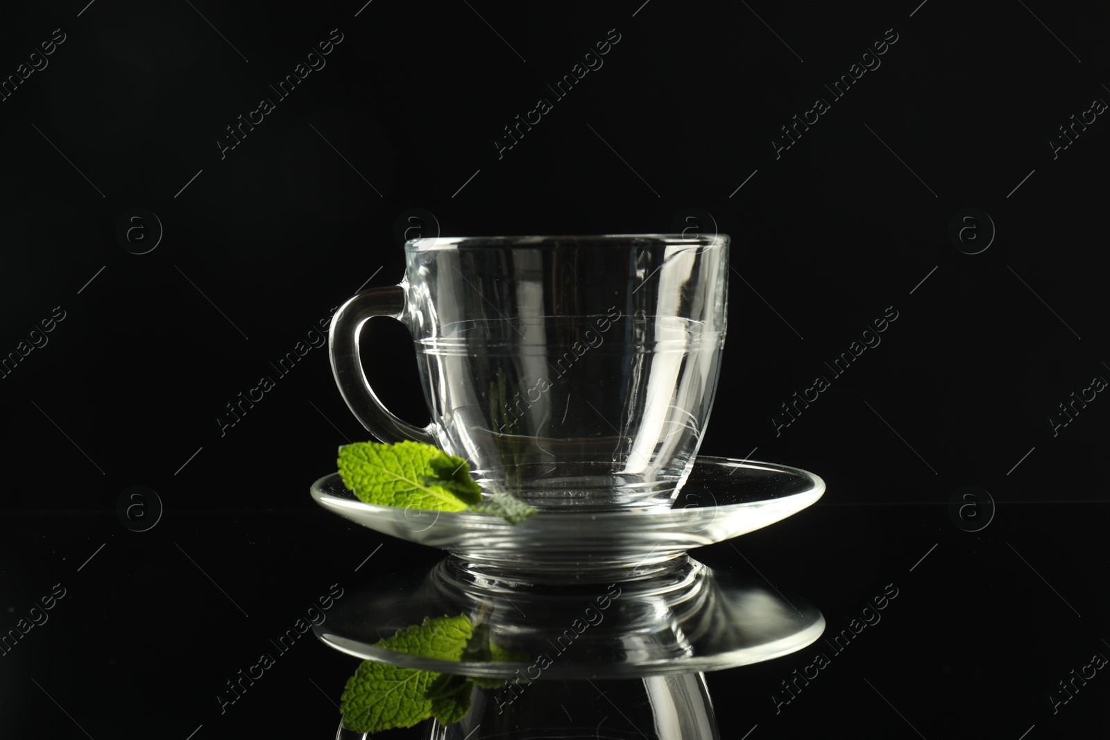 Glass cup, saucer and mint on dark mirror table Photo of Glass cup, saucer and mint on dark mirror table