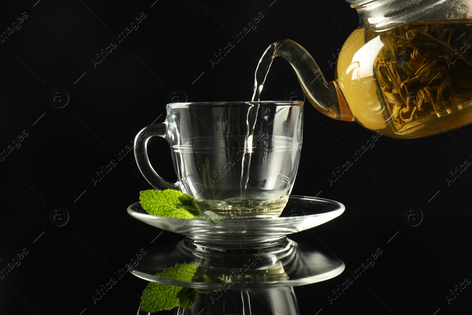 Pouring freshly brewed tea from teapot into cup at dark mirror table, closeup Photo of Pouring freshly brewed tea from teapot into cup at dark mirror table, closeup
