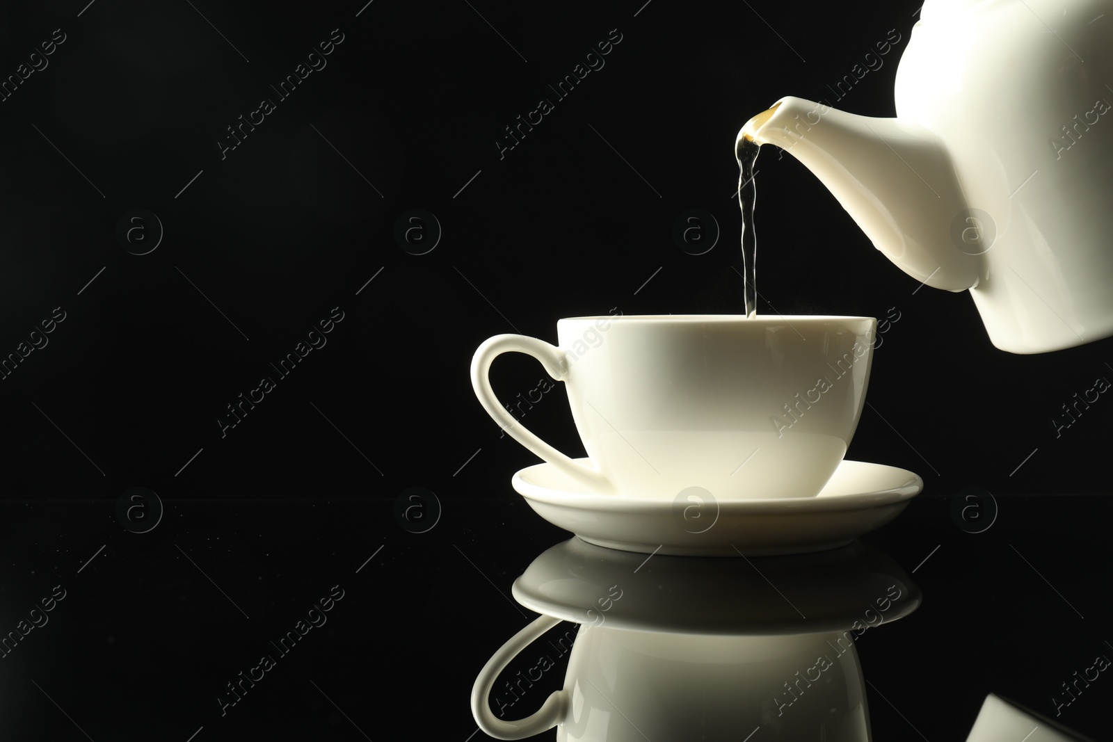 Pouring freshly brewed tea from teapot into cup at dark mirror table, closeup. Space for text Photo of Pouring freshly brewed tea from teapot into cup at dark mirror table, closeup. Space for text