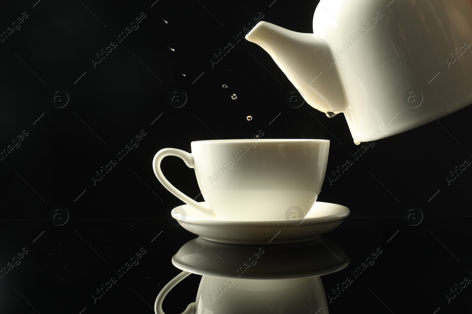 Pouring freshly brewed tea from teapot into cup at dark mirror table, closeup Photo of Pouring freshly brewed tea from teapot into cup at dark mirror table, closeup