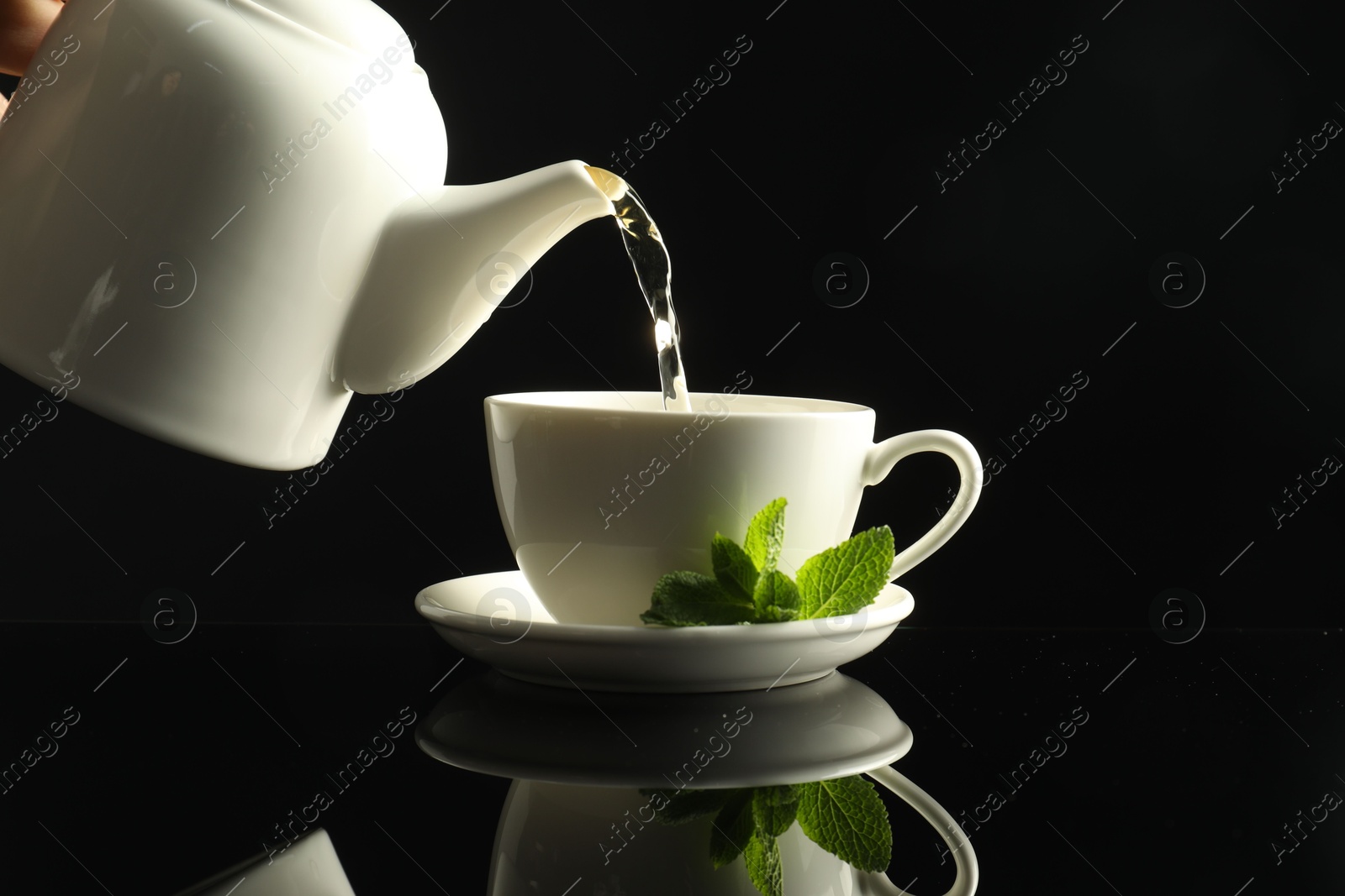 Pouring freshly brewed tea from teapot into cup at dark mirror table, closeup Photo of Pouring freshly brewed tea from teapot into cup at dark mirror table, closeup