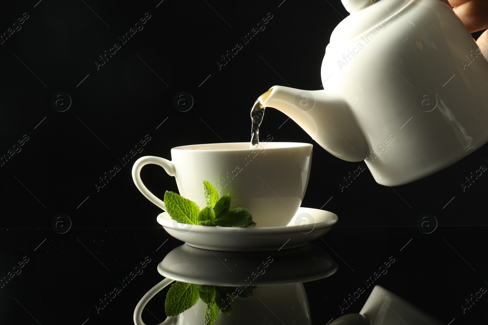 Pouring freshly brewed tea from teapot into cup at dark mirror table, closeup Photo of Pouring freshly brewed tea from teapot into cup at dark mirror table, closeup