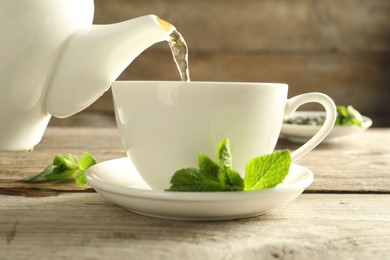 Photo of Pouring freshly brewed tea from teapot into cup at wooden table, closeup