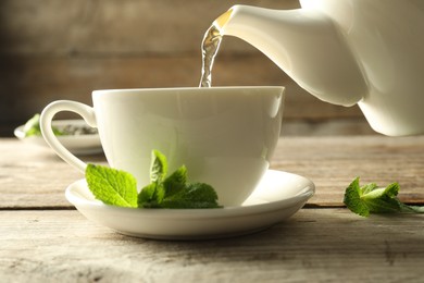 Photo of Pouring freshly brewed tea from teapot into cup at wooden table, closeup