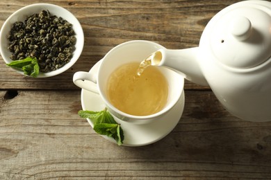 Photo of Pouring freshly brewed tea from teapot into cup at wooden table, above view