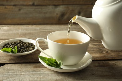 Photo of Pouring freshly brewed tea from teapot into cup at wooden table, closeup