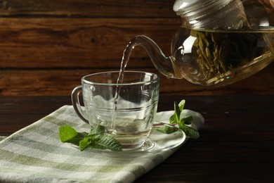 Photo of Pouring freshly brewed tea from teapot into cup at wooden table, closeup