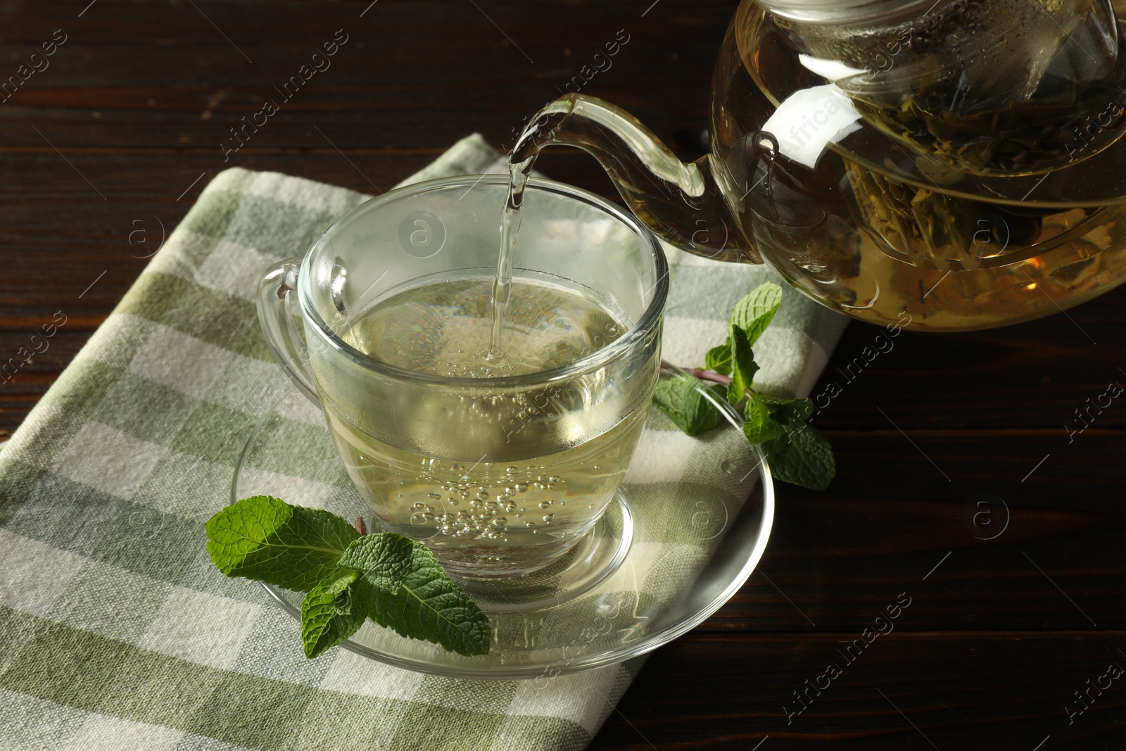 Pouring freshly brewed tea from teapot into cup at wooden table, closeup Photo of Pouring freshly brewed tea from teapot into cup at wooden table, closeup