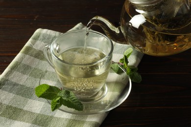 Photo of Pouring freshly brewed tea from teapot into cup at wooden table, closeup