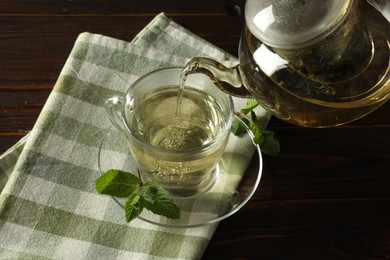 Photo of Pouring freshly brewed tea from teapot into cup at wooden table, closeup