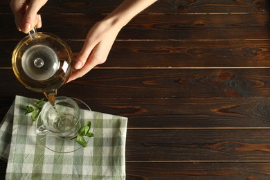 Photo of Woman pouring freshly brewed tea from teapot into cup at wooden table, top view. Space for text
