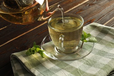 Photo of Pouring freshly brewed tea from teapot into cup at wooden table, closeup