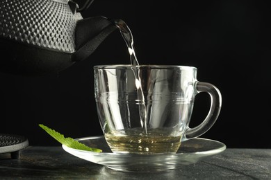 Photo of Pouring freshly brewed tea from teapot into cup at grey table, closeup