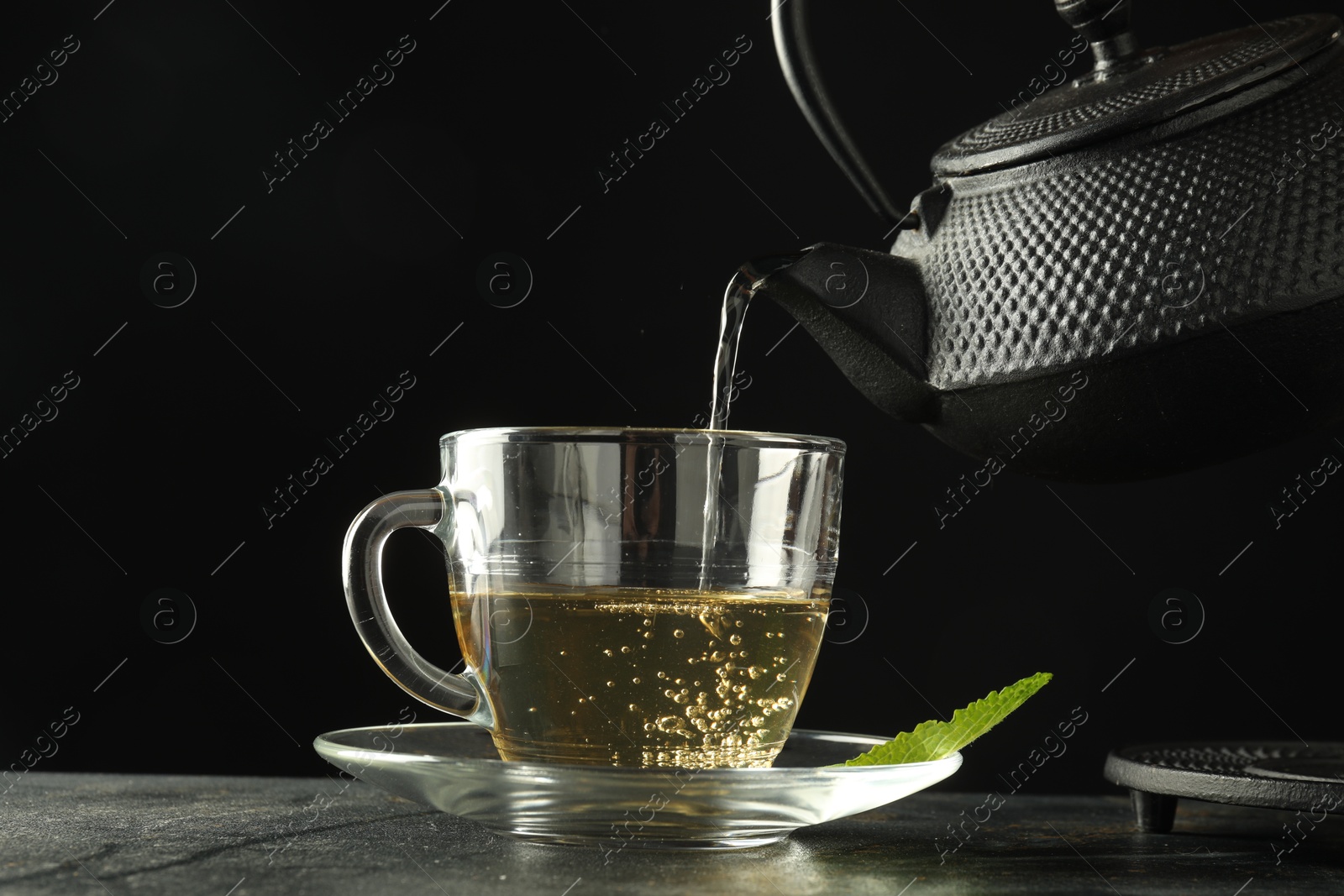 Pouring freshly brewed tea from teapot into cup at grey table, closeup Photo of Pouring freshly brewed tea from teapot into cup at grey table, closeup