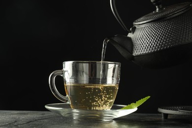 Photo of Pouring freshly brewed tea from teapot into cup at grey table, closeup