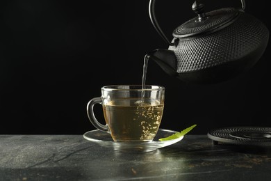 Photo of Pouring freshly brewed tea from teapot into cup at grey table, closeup