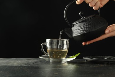 Photo of Woman pouring freshly brewed tea from teapot into cup at grey table, closeup