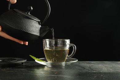 Photo of Woman pouring freshly brewed tea from teapot into cup at grey table, closeup