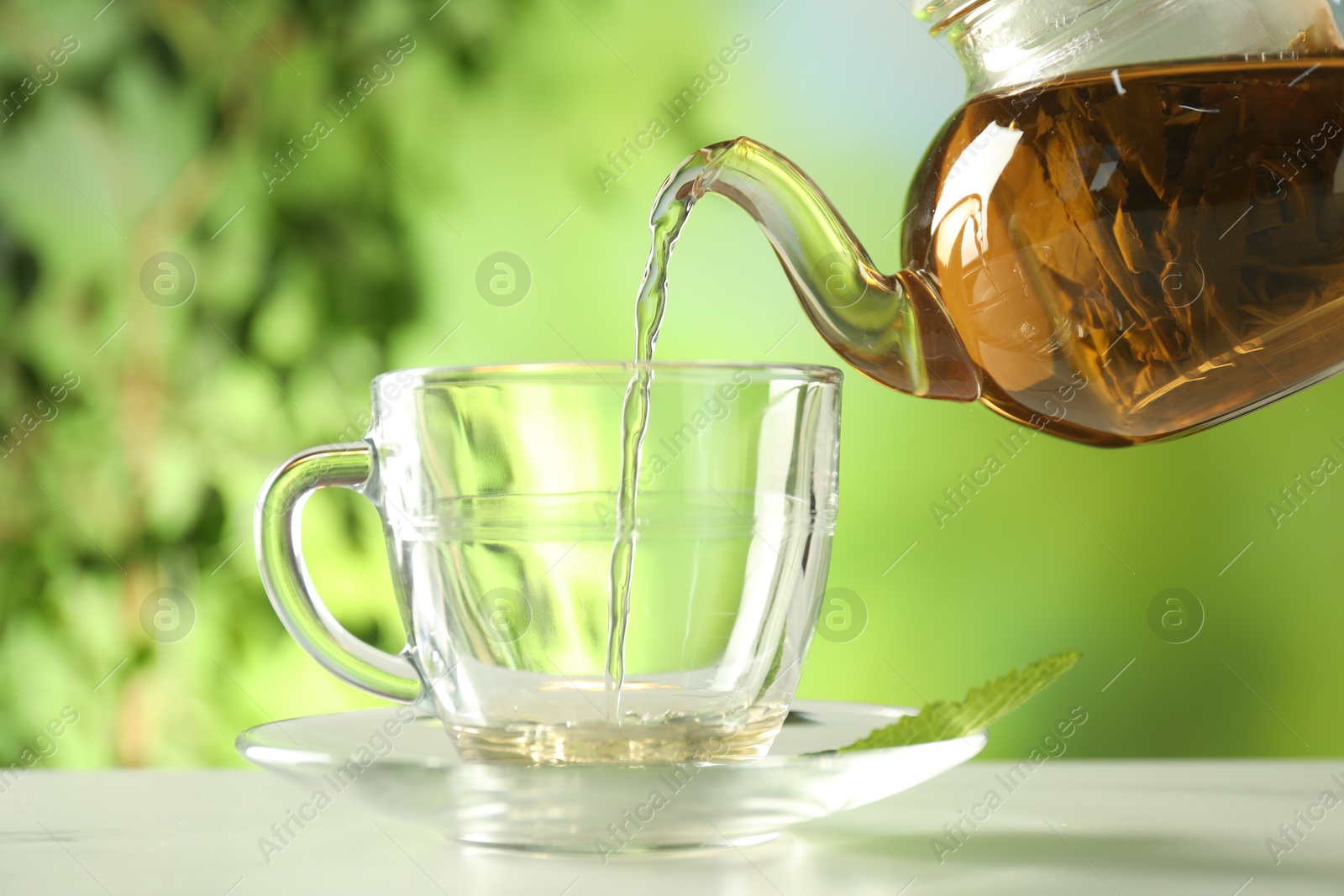 Pouring freshly brewed tea from teapot into cup at white marble table outdoors, closeup Photo of Pouring freshly brewed tea from teapot into cup at white marble table outdoors, closeup