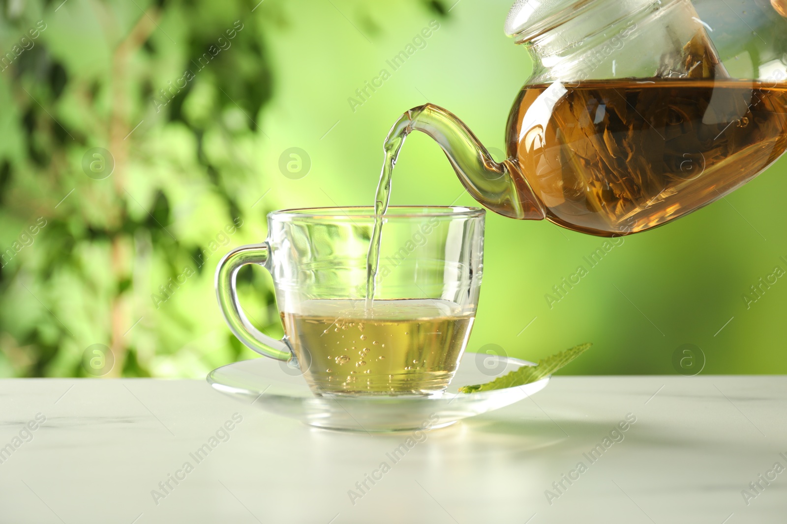 Pouring freshly brewed tea from teapot into cup at white marble table outdoors, closeup Photo of Pouring freshly brewed tea from teapot into cup at white marble table outdoors, closeup