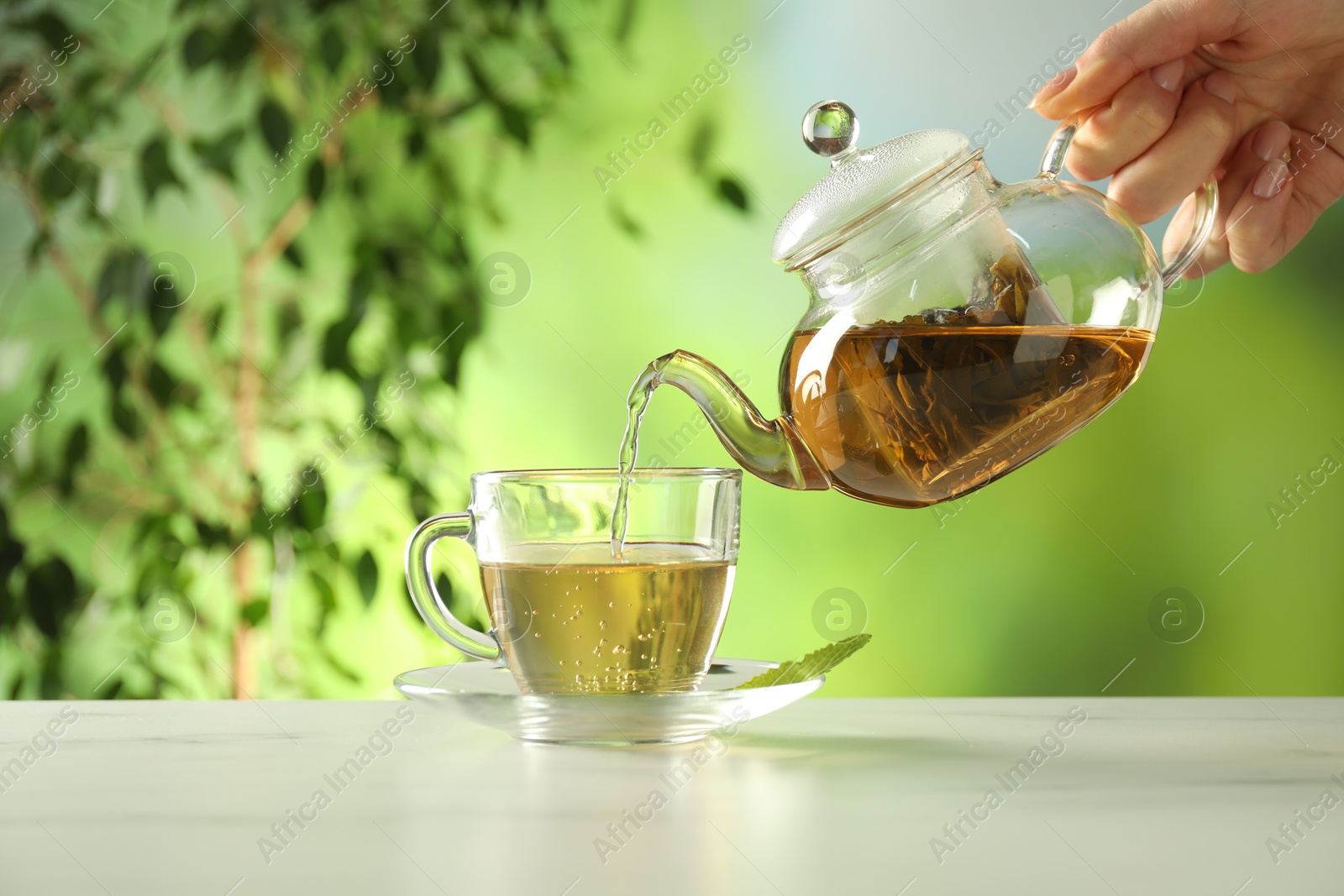Woman pouring freshly brewed tea from teapot into cup at white marble table outdoors, closeup Photo of Woman pouring freshly brewed tea from teapot into cup at white marble table outdoors, closeup