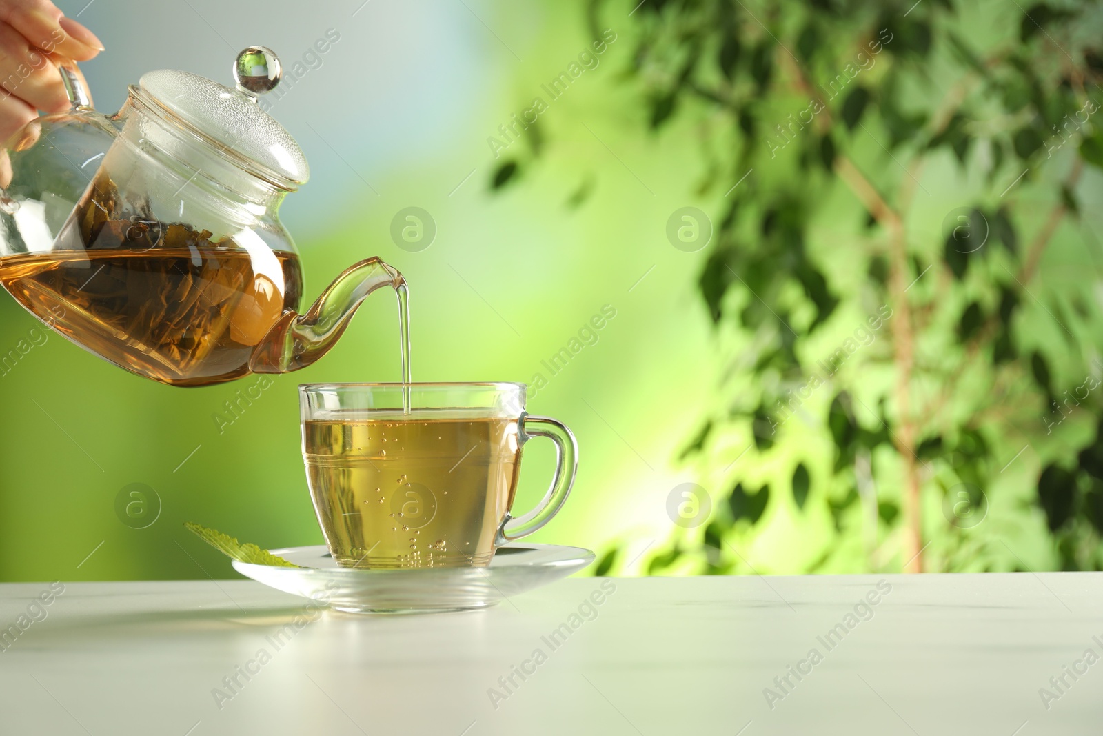 Woman pouring freshly brewed tea from teapot into cup at white marble table outdoors, closeup. Space for text Photo of Woman pouring freshly brewed tea from teapot into cup at white marble table outdoors, closeup. Space for text