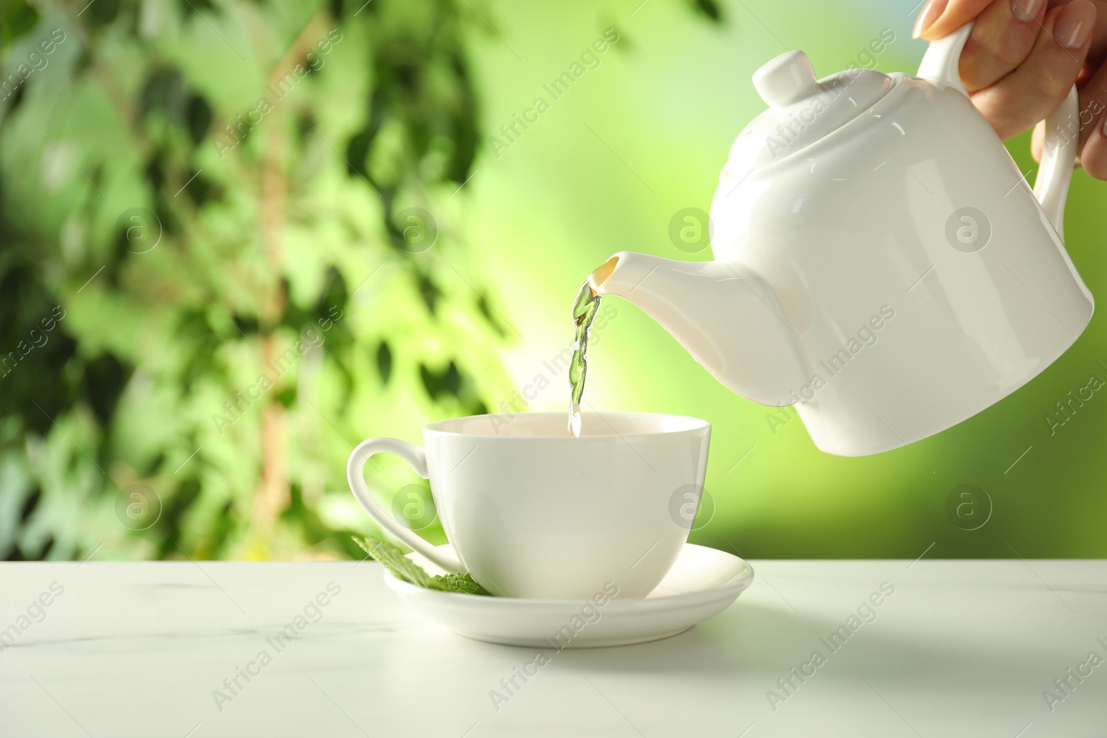 Woman pouring freshly brewed tea from teapot into cup at white marble table outdoors, closeup Photo of Woman pouring freshly brewed tea from teapot into cup at white marble table outdoors, closeup