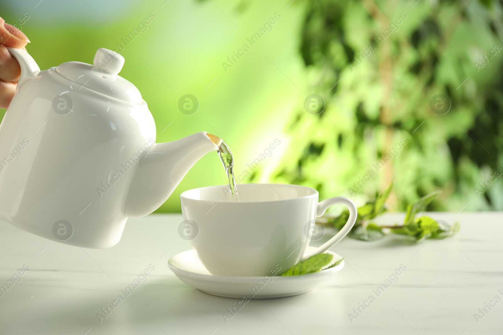 Woman pouring freshly brewed tea from teapot into cup at white marble table outdoors, closeup Photo of Woman pouring freshly brewed tea from teapot into cup at white marble table outdoors, closeup