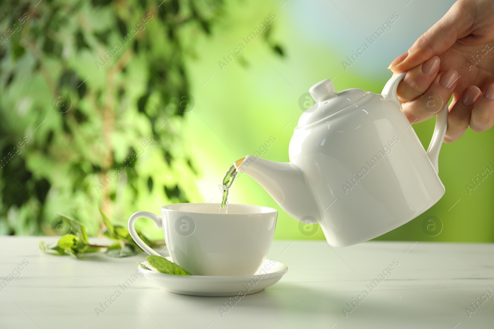 Woman pouring freshly brewed tea from teapot into cup at white marble table outdoors, closeup Photo of Woman pouring freshly brewed tea from teapot into cup at white marble table outdoors, closeup